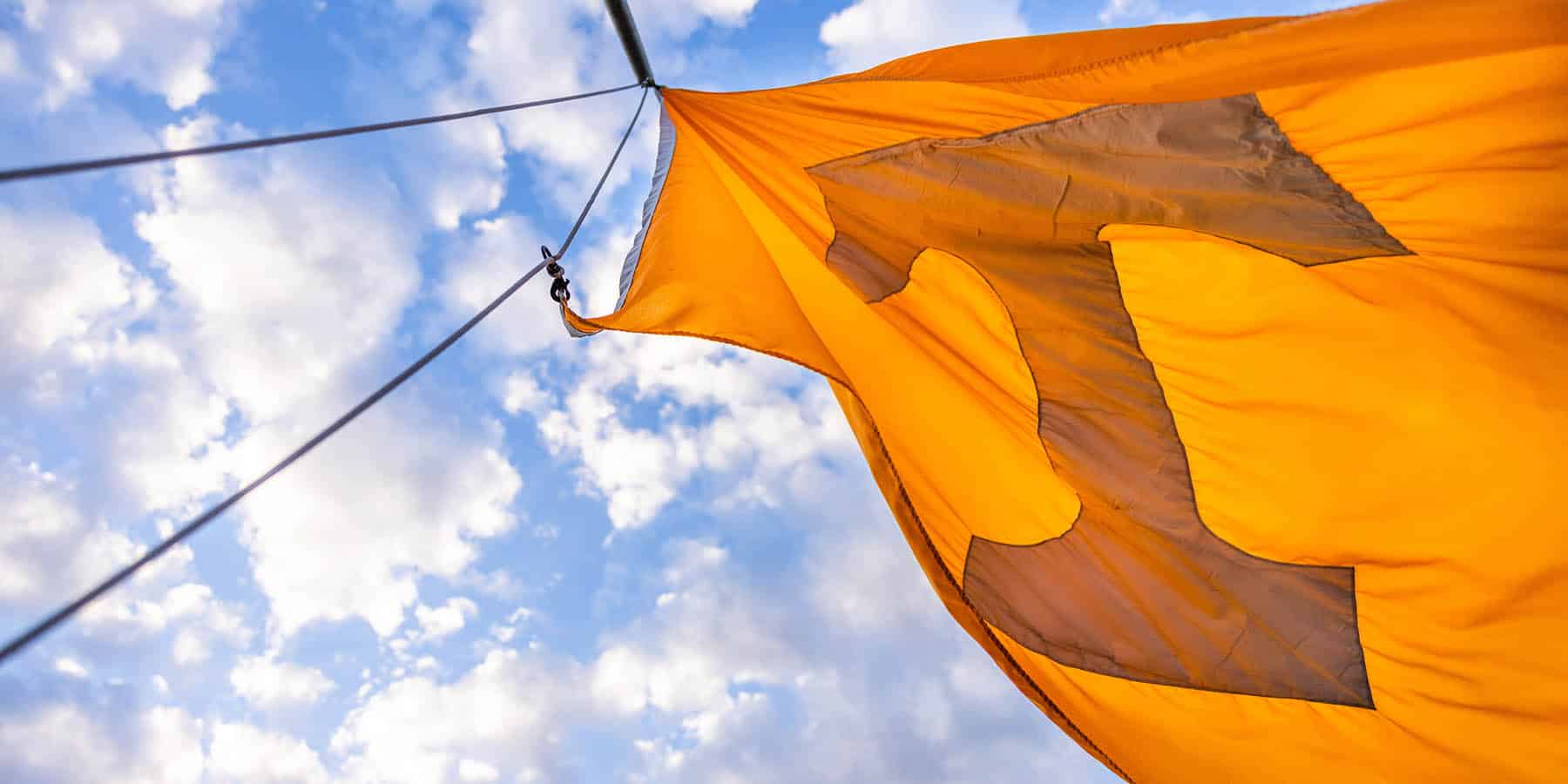 An orange Power T flag waves in the wind with blue skies behind it. Photo by Steven Bridges.