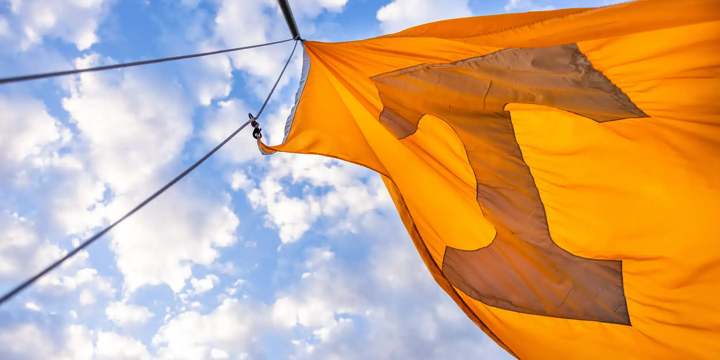 An orange UT flag flying in the wind on a clear day